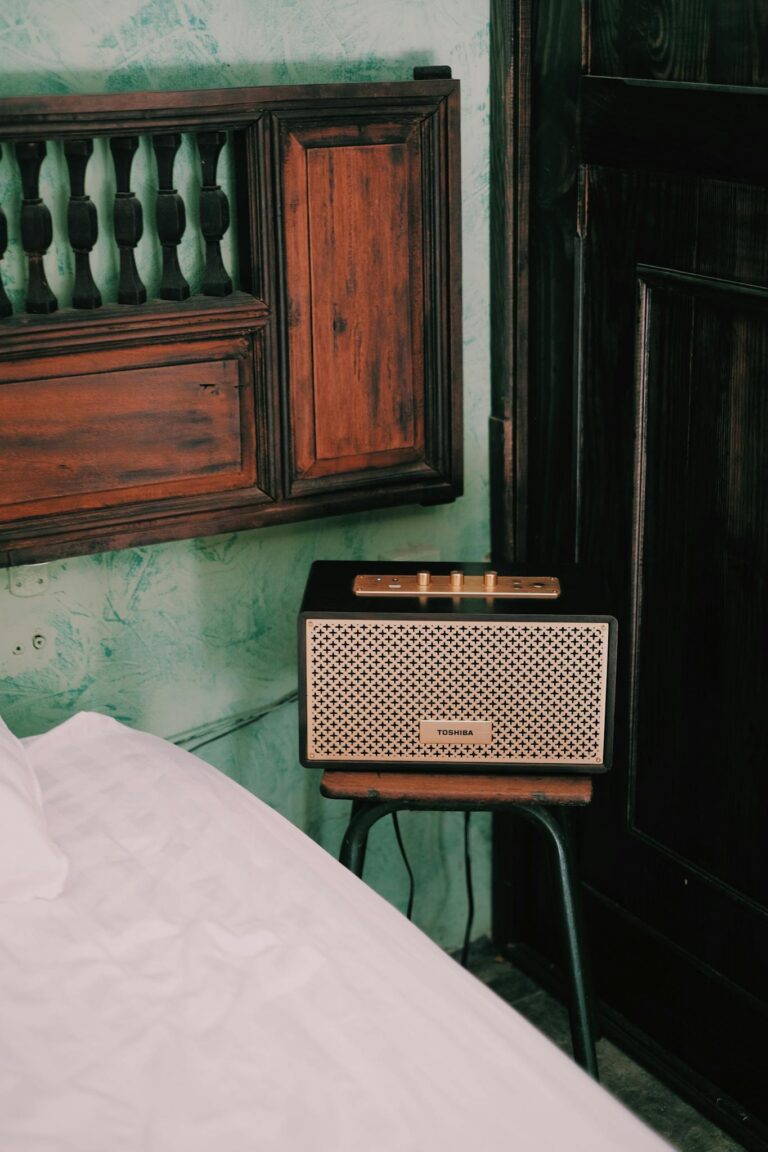 A retro radio resting on a stool beside a bed in a rustic bedroom setting.